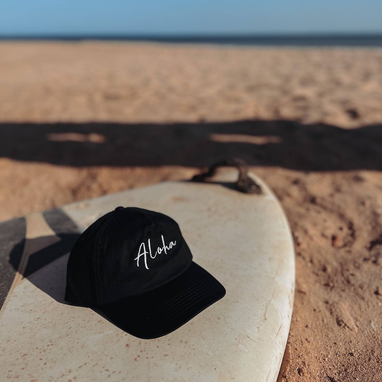 Aloha Cap auf Surfbrett – Der Spirit von Hawaii inspirierter Kleidung am Strand