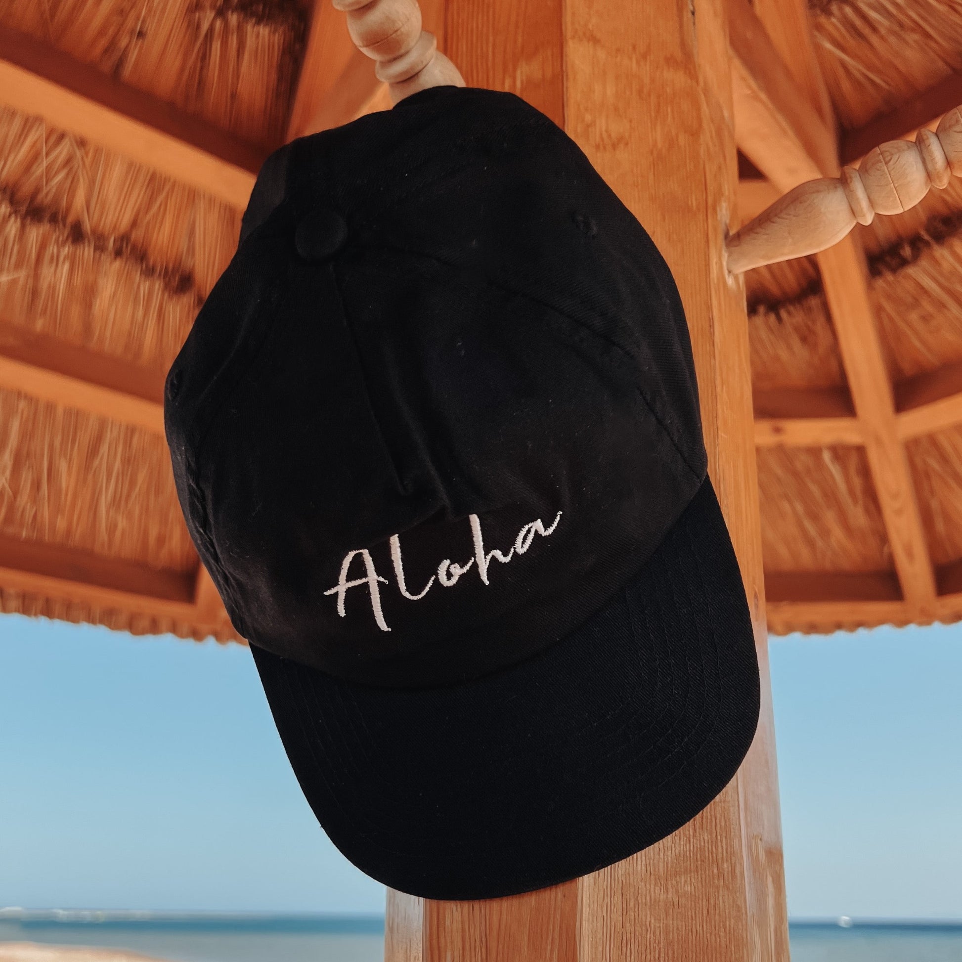 Aloha Cap hängend am Schirm – Essential für das Strandurlaub Outfit